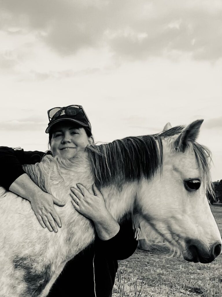 Black and white image of Kelly hugging a horse and smiling. 