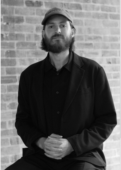 Black and white portrait of Luke de Silva with hands clasped in his lap. 